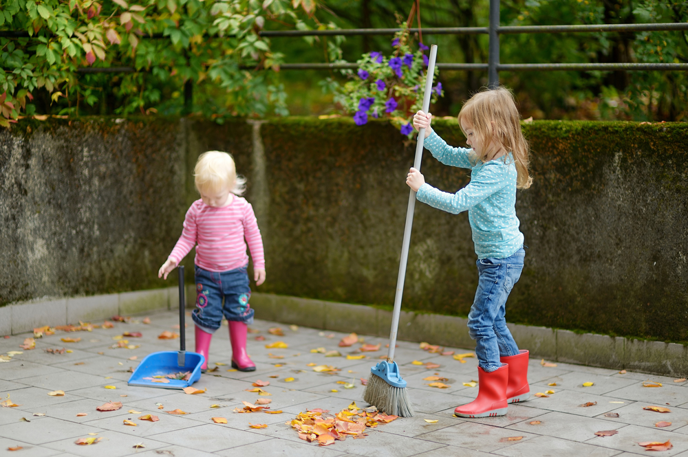 Cute little girls sweeping dry yellow leaves on autumn day